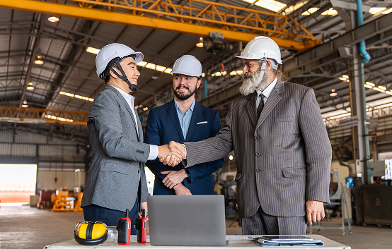 Three engineers shaking hands in a factory.