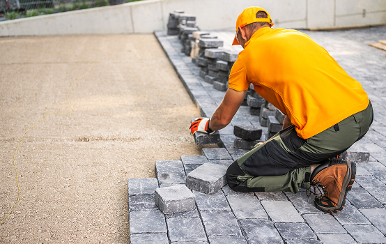 Worker laying gray paving stones outdoors.